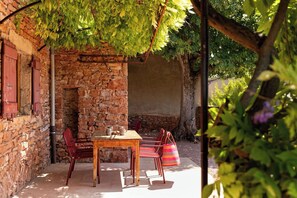Eine Außenpatio mit einer Steinmauer, einem Holztisch, roten Stühlen und einer hängenden Pflanze.