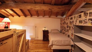 Ein Schlafzimmer mit Holzbalkendecke, einem Bett mit weißer Bettdecke, einem Nachttisch mit Lampe und einer Wand voller Fotos.