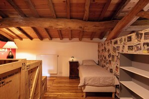 A bedroom with a wooden ceiling, a bed with a white bedspread, a nightstand with a lamp, and a wall covered with photographs. - Maison Pourpre | Sleeps 10 | Burgundy | Close to the village (Leynes)