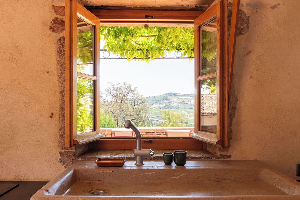 A window with a view of a landscape, a sink with a faucet, and two cups on the windowsill.