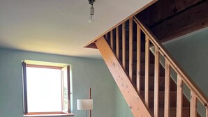 Ein Zimmer mit einer Holztreppe, einem großen Fenster, einer Stehlampe und einem dunklen Holzschrank.