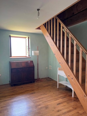 A room with a wooden staircase, a large window, a floor lamp, and a dark wooden cabinet. - Maison Pourpre | Sleeps 10 | Burgundy | Close to the village (Leynes)