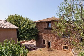 Ein Steinhaus mit Ziegeldach, einem kleinen Fenster und einer Tür. Es gibt eine Terrasse mit Gartenmöbeln.