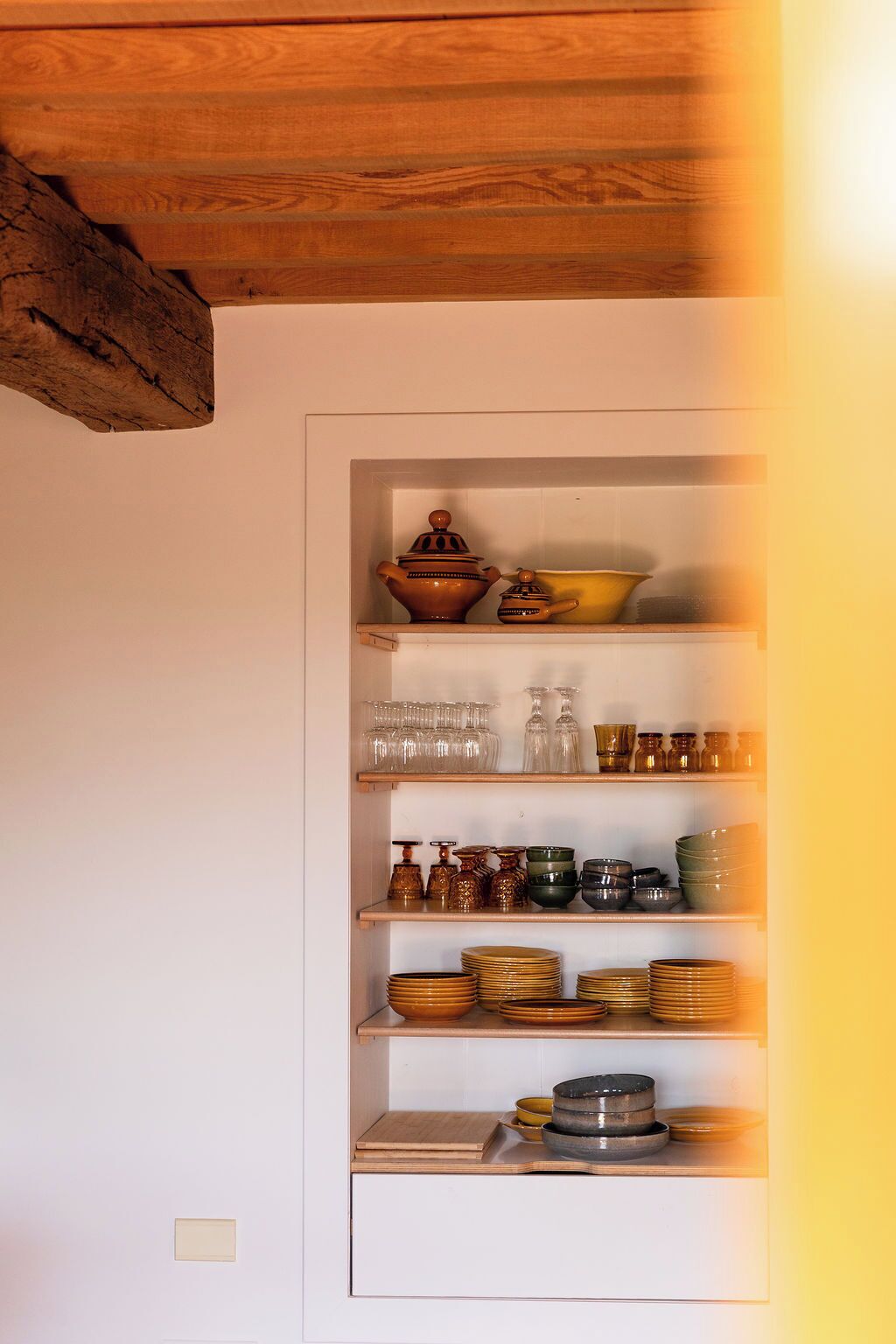 Una cucina con travi in legno, scaffali pieni di utensili da cucina e una parete bianca.