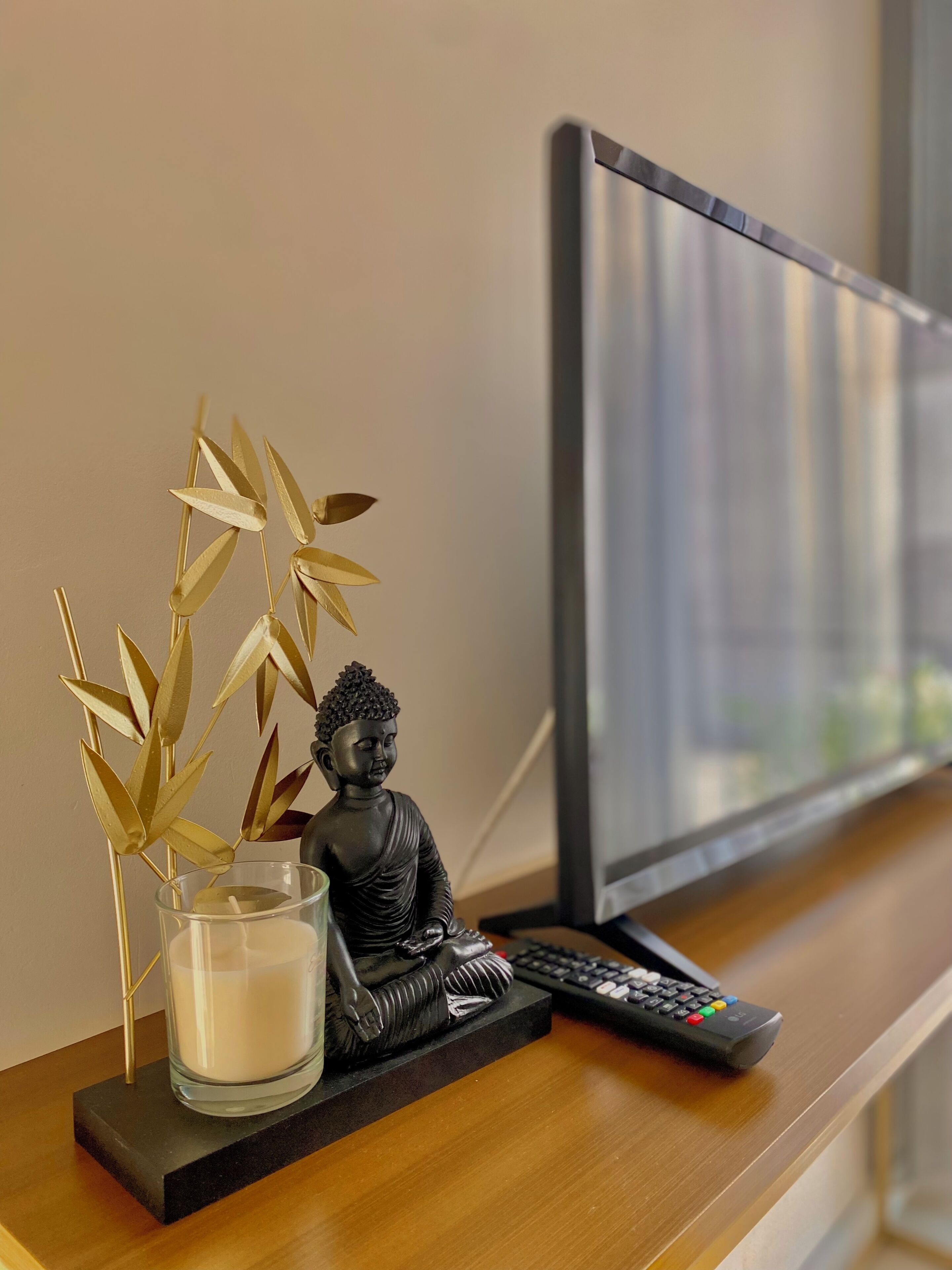 Una statua di Buddha, una candela e un telecomando su una scrivania di legno.