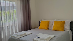 A neatly made bed with a grey bedspread, two yellow pillows, and a white headboard. - Casinha dos Carris- AL (Valença)