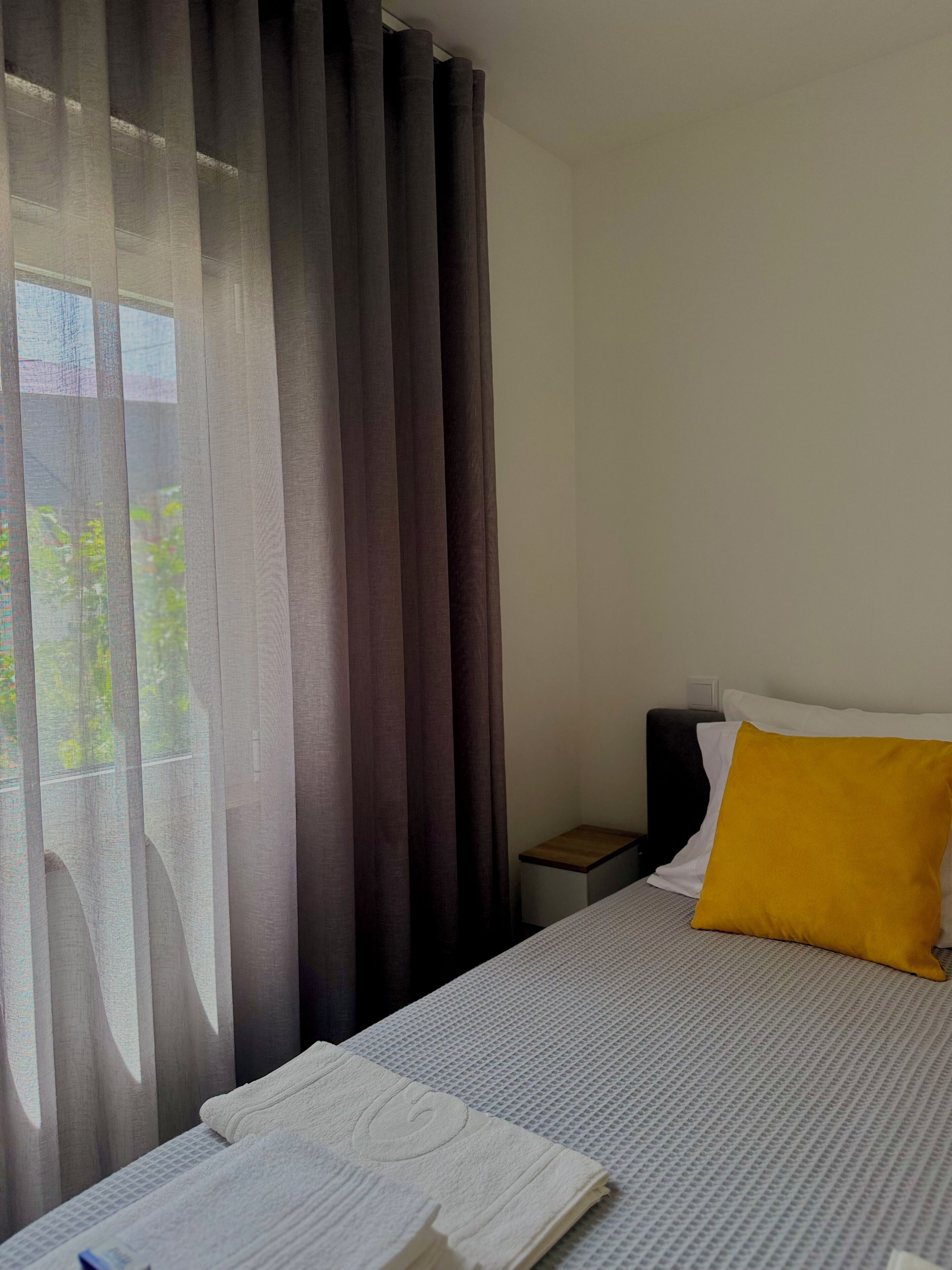 Una camera d'hotel con un letto, un comodino, una lampada e una finestra con tende.