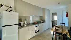 A modern kitchen with a refrigerator, microwave, stove, and oven. There is a dining table with chairs and a window providing natural light. - Casinha dos Carris- AL (Valença)
