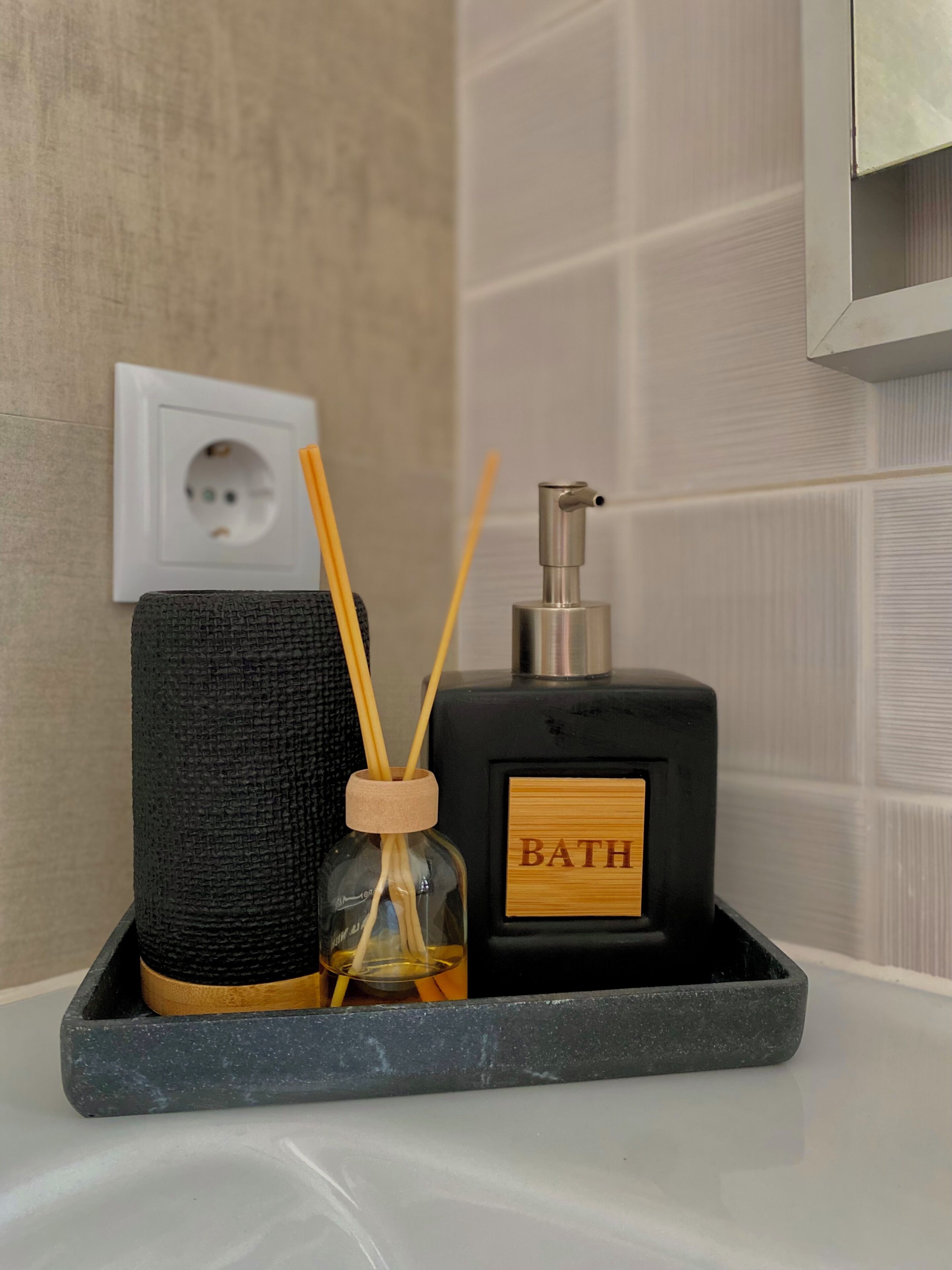 A bathroom with a black diffuser, a bottle labeled 'BATH,' and a glass container with reed sticks.