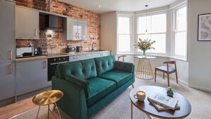 A modern kitchen with a brick wall, a green sofa, and a dining area with a round table. - Umpires Watch - Cricket View - Free Parking (Scarborough)