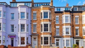 A row of terraced houses with distinct architectural styles, including a purple building with a sign 'The Boundary' and a corner house with a brick facade. - Umpires Watch - Cricket View - Free Parking (Scarborough)