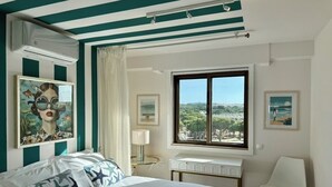 Ein Schlafzimmer mit Bett, Schreibtisch, Stuhl, einem Fenster mit Blick und Bildern an der Wand.