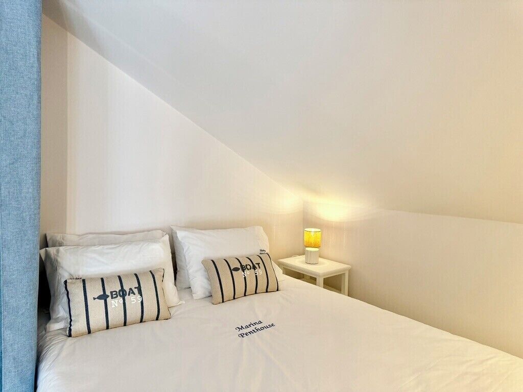 Un lit bien fait, avec deux oreillers, une lampe de chevet et une étagère fixée au mur.