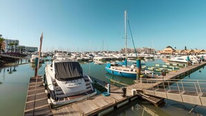 Un puerto deportivo con varias embarcaciones amarradas, un muelle de madera y un cielo azul despejado.