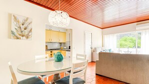 Una sala moderna con una mesa de comedor de vidrio, sillas blancas, un sofá y vistas al exterior.