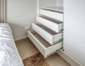 Et soveværelse med en seng, en hvid væg og et indbygget hvidt opbevaringsmøbel med skuffer.