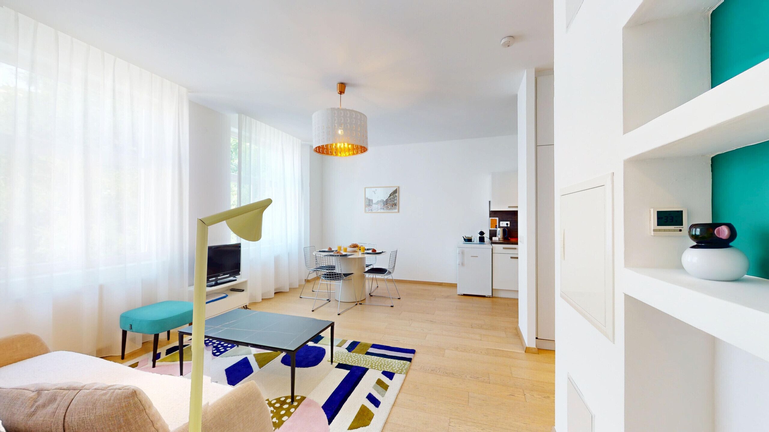 A modern living room with a sofa, a dining table, a TV, and a kitchen in the background.