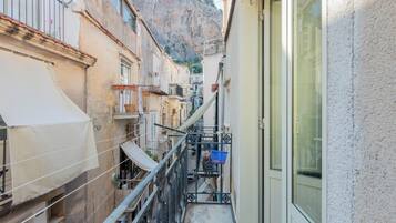 Eine schmale Stadtstraße mit Gebäuden, einem Balkon und einem Berg im Hintergrund.