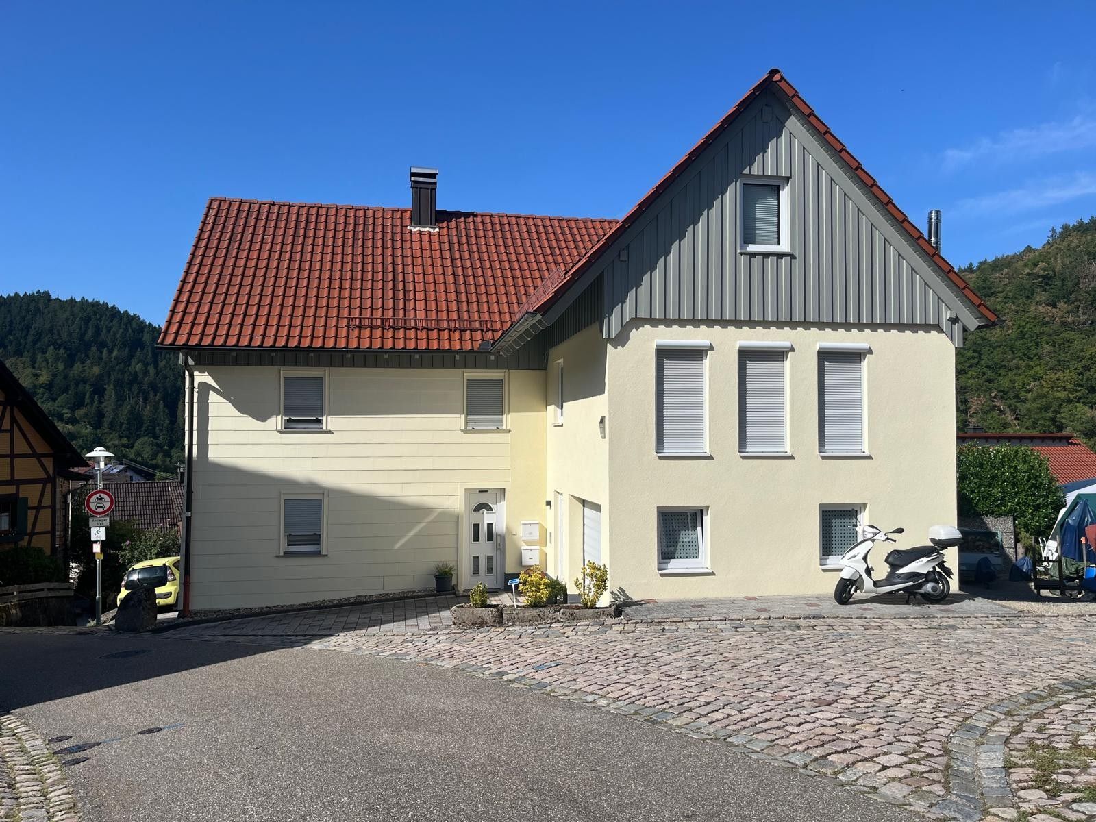 Ein zweistöckiges Gebäude mit rotem Ziegeldach, einem kleinen Balkon und einem abgestellten Roller.