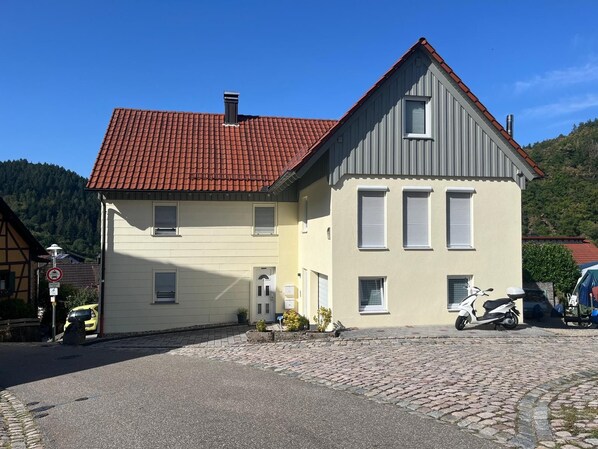 Ein zweistöckiges Gebäude mit rotem Ziegeldach, einem kleinen Balkon und einem abgestellten Roller.