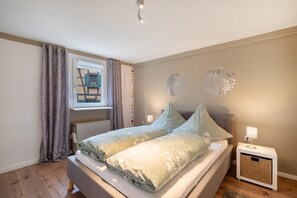 Un dormitorio con cama, una mesita de noche con lámpara, una ventana con cortinas y un adorno en la pared.