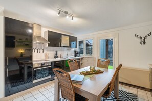 Cocina moderna con comedor, que incluye horno empotrado, electrodomésticos de acero inoxidable y una mesa con sillas de mimbre.
