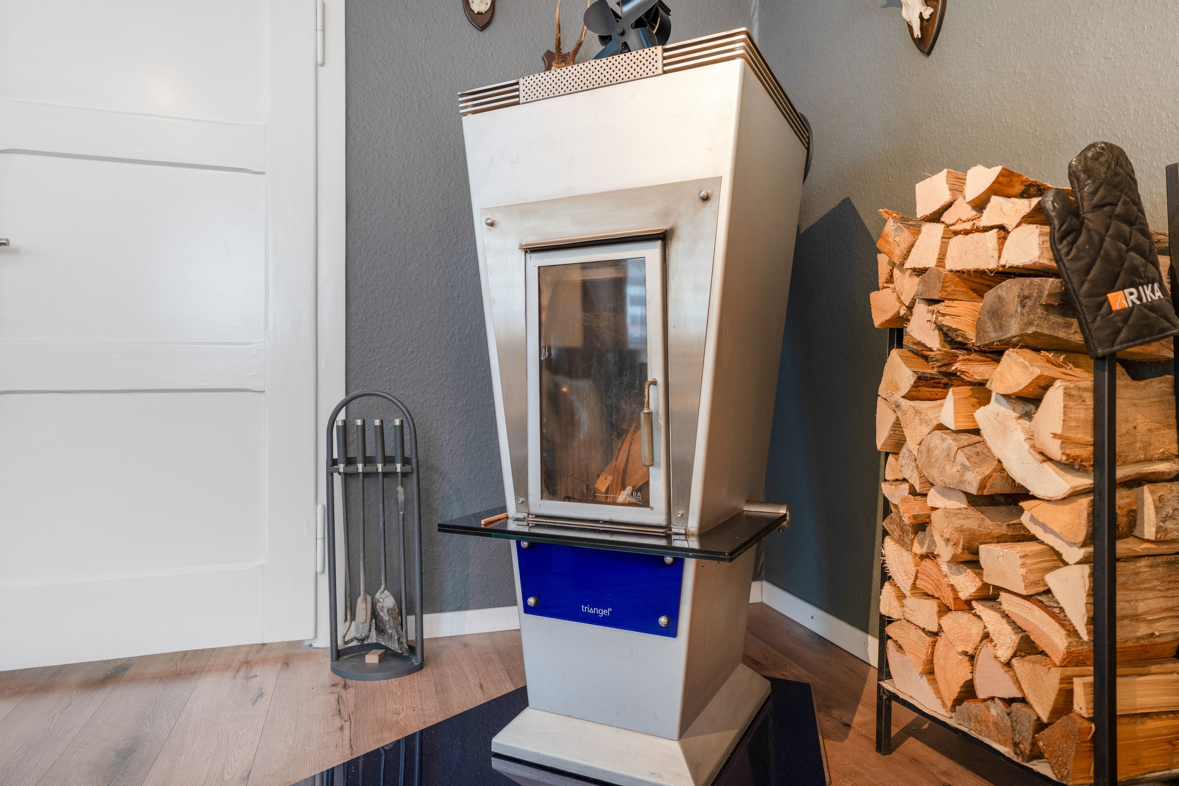 Un poêle à bois doté d’une porte en verre, d’un support métallique pour les bûches et d’un radiateur métallique posé sur un plancher en bois.