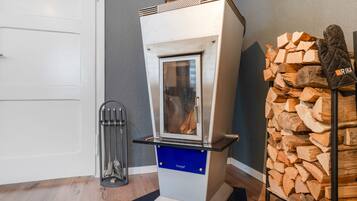 Ein Holzofen mit Glastür, ein Metallregal mit Holzscheiten und ein Metallheizkörper auf Holzdielen.