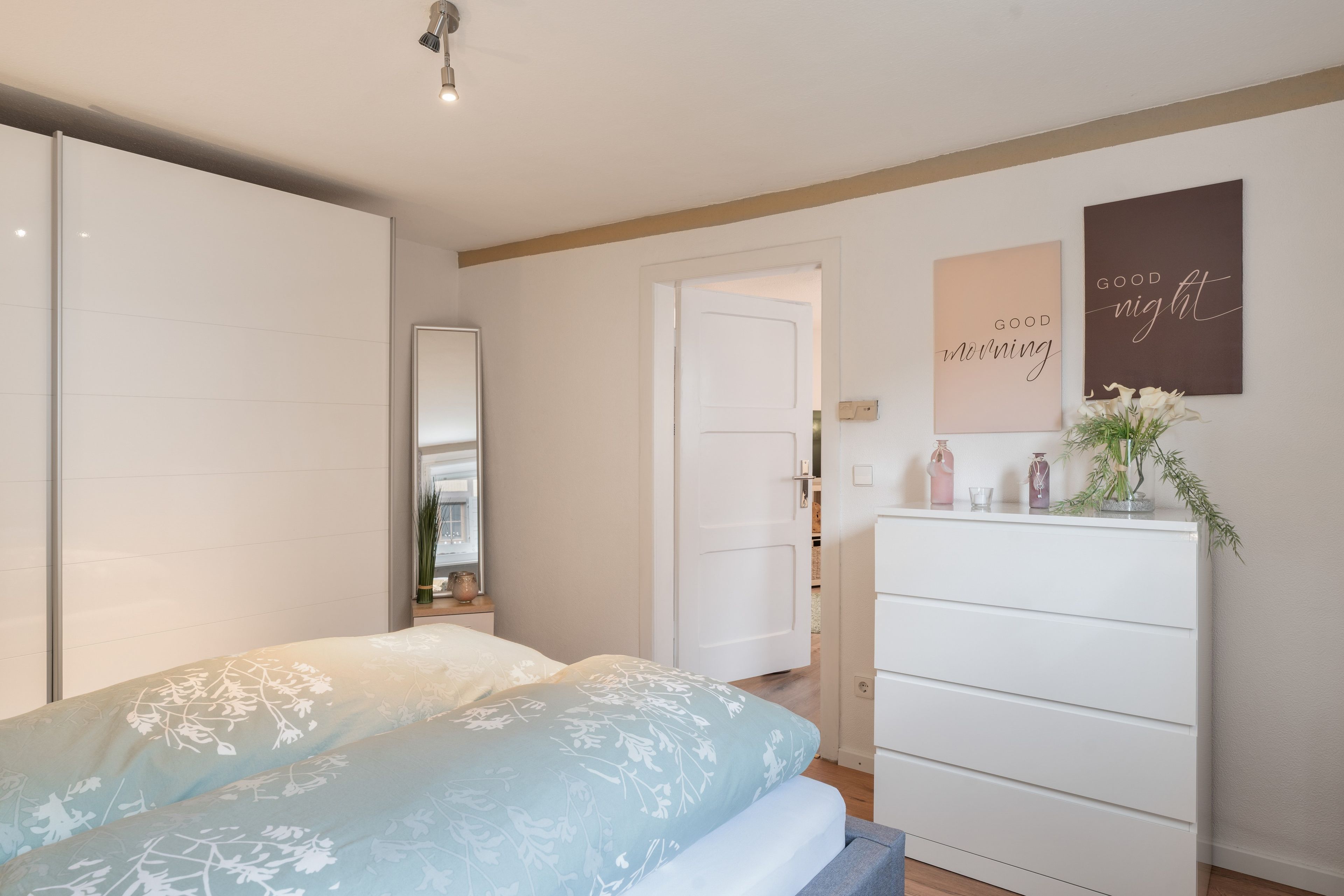 Ein Schlafzimmer mit Bett, Schminktisch und einer Tür zu einem anderen Raum.