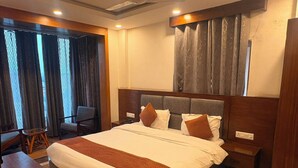 Habitación de hotel con una cama grande, un escritorio, dos sillas y un ventanal con cortinas.