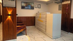 Zona de recepción con un mostrador de madera, un cartel de recepción, cuadros en la pared y una escalera.