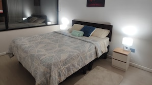 Ein Schlafzimmer mit Bett, Nachttischlampen, einem Nachttisch, einem Fenster und einem Wandbild.