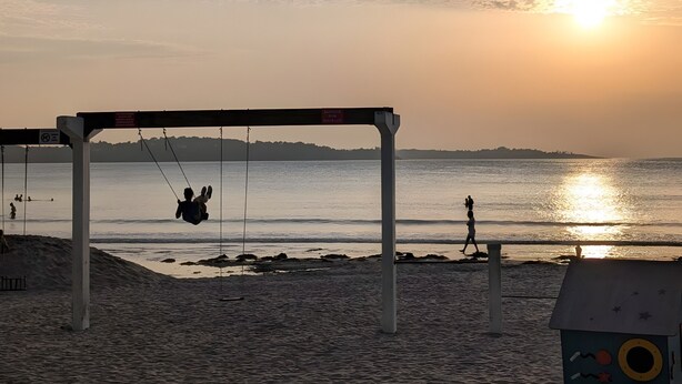 A beach with a swing set, a lifeguard tower, and a sunset in the background.