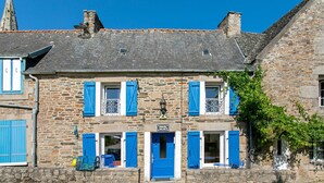 A stone building with blue shutters, a central door, and a small sign above the door.