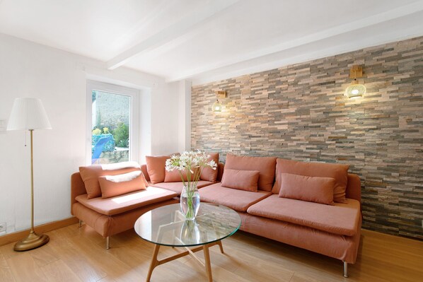 A modern living room with a glass coffee table, a pink sofa, a stone wall, and a floor lamp.