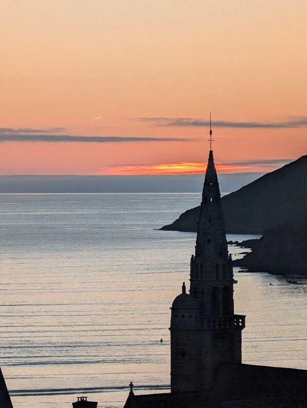 A coastal church with a tall spire, overlooking the sea.