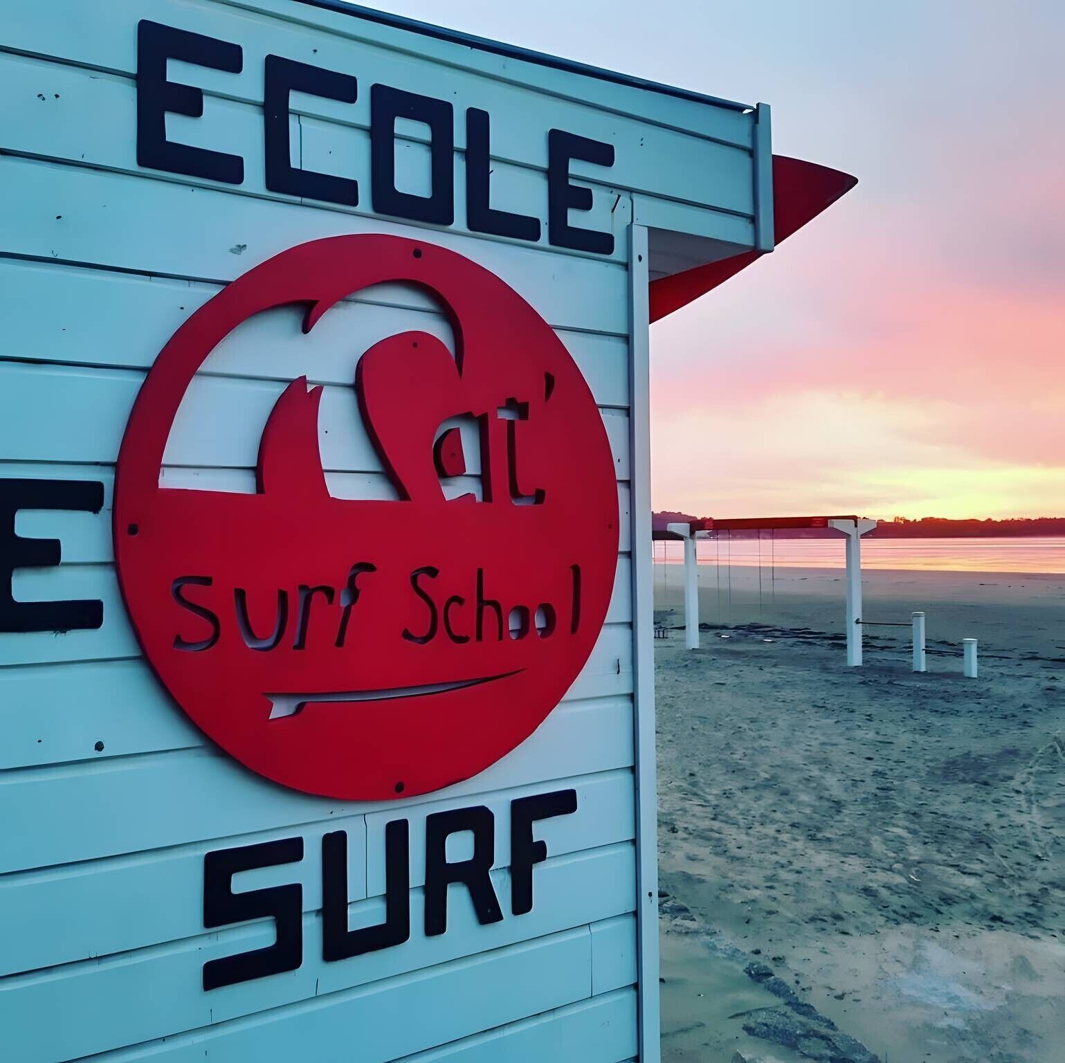 Señal de una escuela de surf con un logotipo rojo y las palabras 'Ecole' y 'Surf School' sobre un fondo blanco.