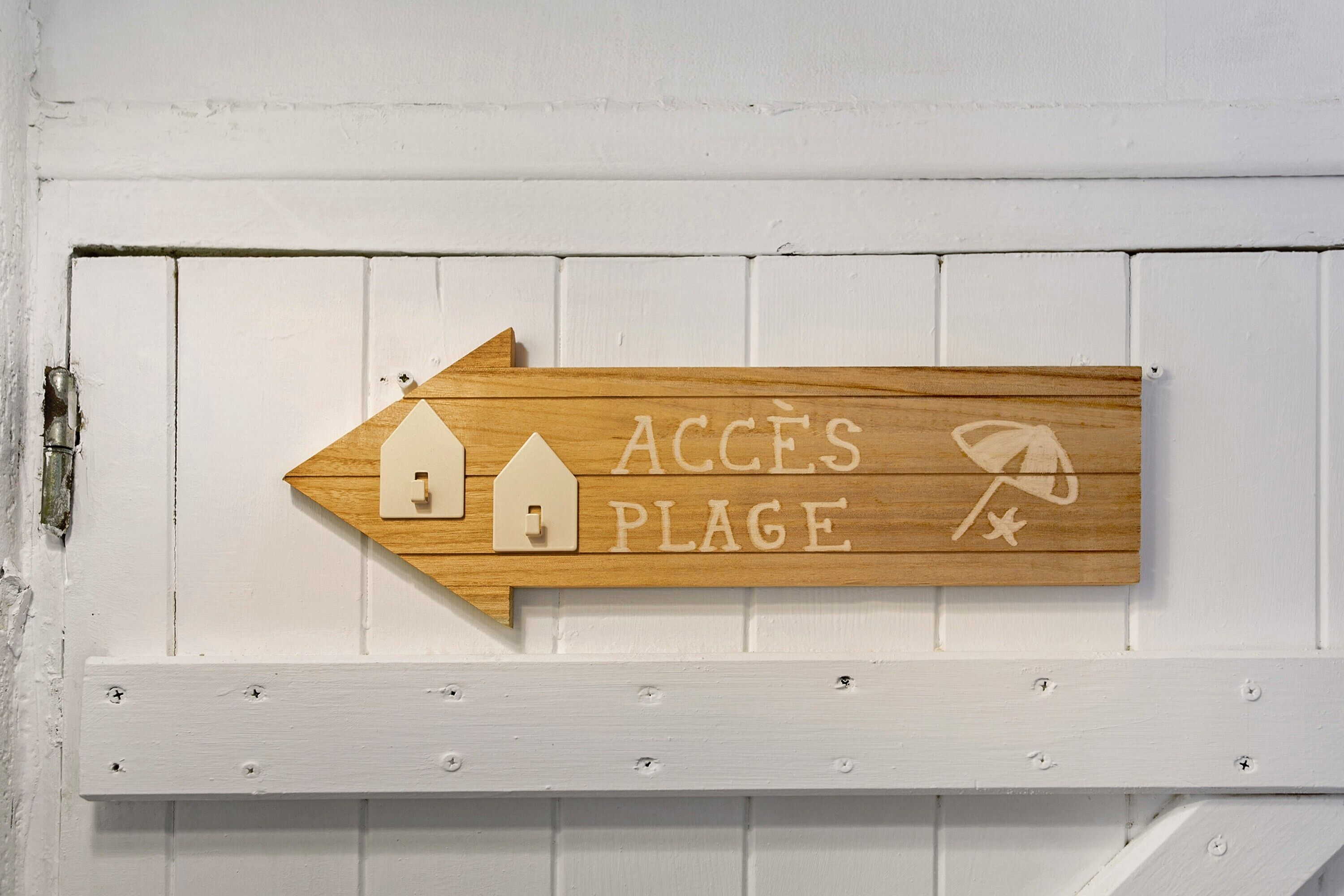 A wooden sign with a house and a star symbol, indicating access to a beach.