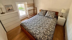 A bedroom with a bed, bedside tables, a hanging clothes rack, a window, and a door.