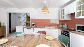 Une cuisine moderne avec des meubles blancs, une table à manger en bois mise avec des assiettes et des verres, et un luminaire suspendu.