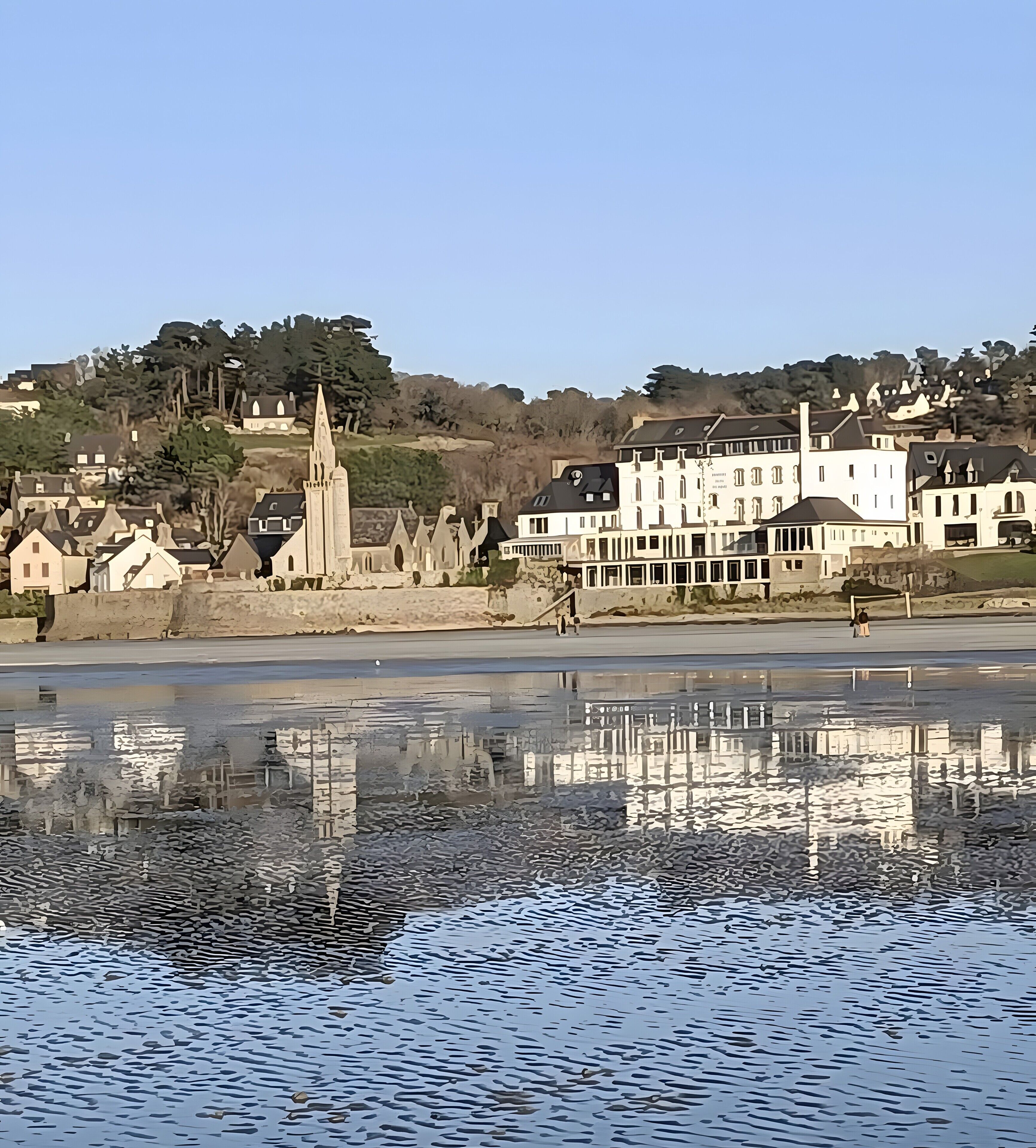 A waterfront view with buildings and a church, reflecting in calm water.