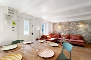 Un salon moderne avec un coin repas, comprenant un mur en pierre, un ensemble de canapés et une table à manger en bois agrémentée de sets de table et de verres à vin.