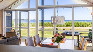 Een modern interieur met grote ramen, een eethoek en uitzicht op het water.