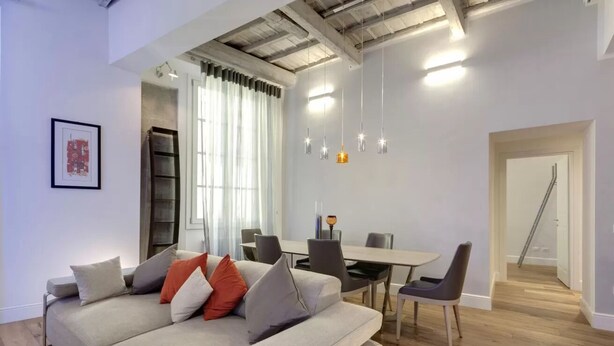 Ein modernes Wohnzimmer mit einer Couch, einem Esstisch, Stühlen, Pendelleuchten und einer Treppe.