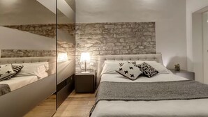 Ein Schlafzimmer mit Steinsturz, einem Bett mit weißer Bettwäsche, einem Nachttisch mit Lampe und einem Spiegel.