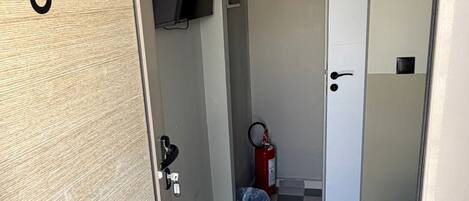 A small room with a checkered floor, a television mounted on the wall, a fire extinguisher, and a door labeled '8olon'.