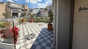 A rooftop terrace with a checkered floor, green chairs, potted plants, and a view of surrounding buildings. - Petite rooftop room for 1person (ATHENS)