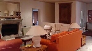Un salon avec une cheminée, un canapé orange, deux lampes et un coin repas.