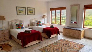 Quarto com duas camas, uma mesa de cabeceira, cômoda, espelho e janela com vista.