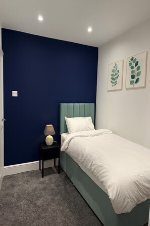 A bedroom with a single bed, a bedside table with a lamp, and two framed leaf artworks on the wall.